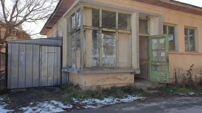 Close-up of the bakery corner featuring large windows, a green door, and surrounding dry grass with snow patches.