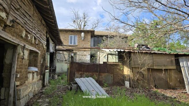 The rear yard area with old outbuildings made of wood and metal sheets, and the back of the two-storey house with windows and doors.