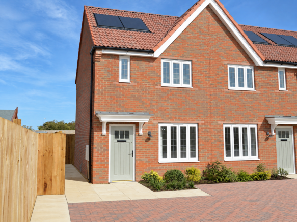 A two-story red brick house with white-framed windows and grey doors sits behind a paved driveway an