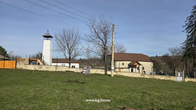 View of a white bell tower and a fenced house situated on a grassy hill with trees around.