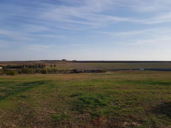 Expansive grassy field with the farm building visible far away, under a clear blue sky.