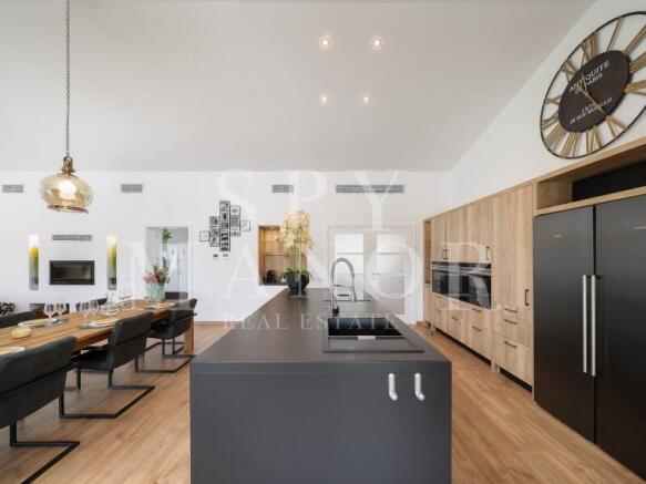Modern fully fitted kitchen and open-plan dining area inside a brand new luxury single-storey villa for sale in Estômbar, Algarve, featuring a dark kitchen island and wood cabinetry.