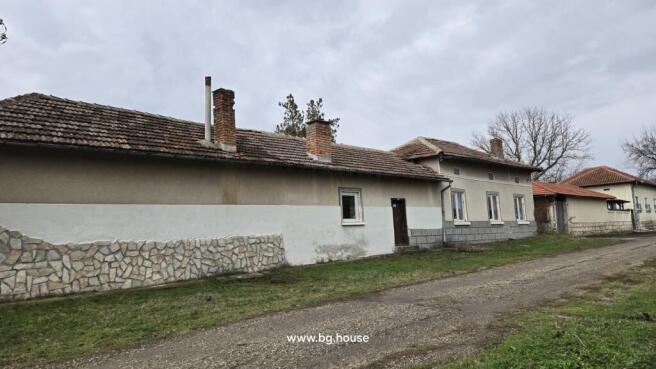 Side facade of a Bulgarian house showing multiple chimneys, windows, and a dirt road alongside the building.