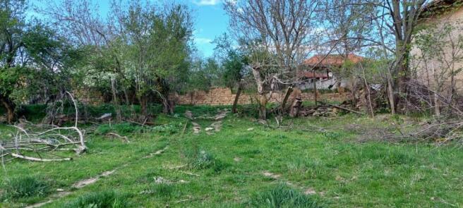 Grassy land showing dirt tracks leading to a stone wall surrounded by trees, with houses visible beyond the wall.