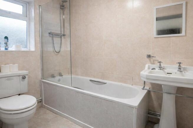 Bright, clean tiled bathroom with a bath and ov...