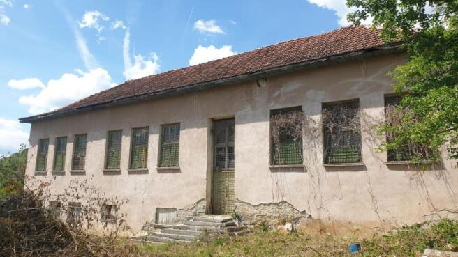 Facade of the old school showing barred windows, tiled roof, and gated entrance with steps