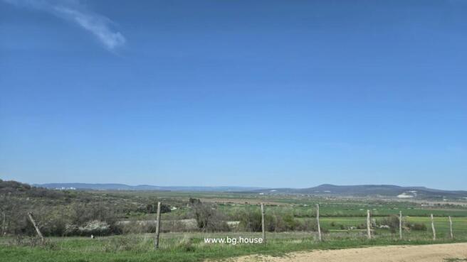 Expansive view of rural fields and hills under a clear blue sky with a dirt road and wooden fence posts in the foreground.