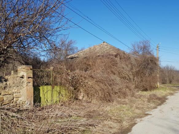 Side view of an old house with a green metal gate and dry vegetation around