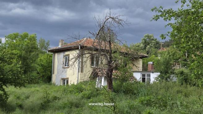 Exterior view of a two-storey yellow house with a tiled roof and surrounding greenery in Koprivets village.