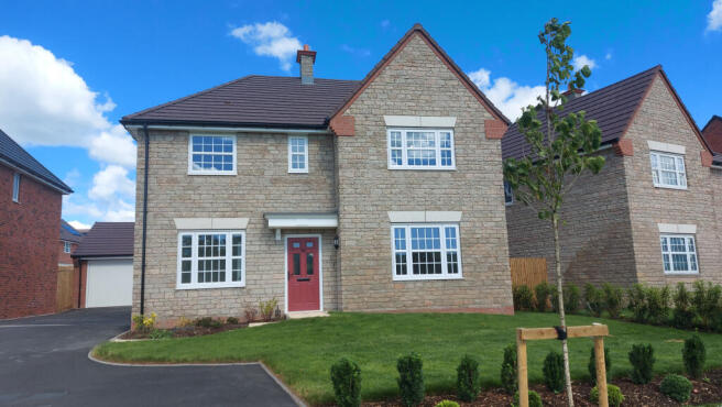 A modern stone house with a red door sits on a manicured lawn in the foreground