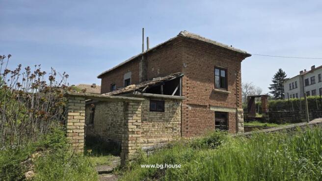 Side perspective of the house showing brick walls, annex, windows, and surrounding green plants