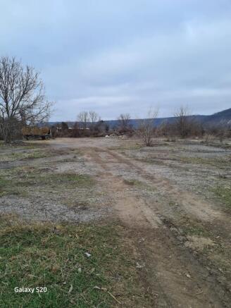 Open dirt and gravel land with scattered bare trees and a hay wagon parked on the left side under a cloudy sky.