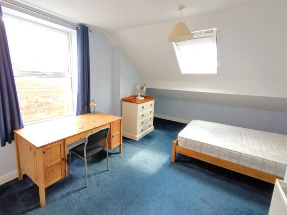 Bright attic bedroom with a large desk by a win...