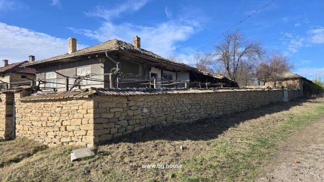 Stone wall enclosing a traditional Bulgarian house with tiled roof and chimney under clear blue sky