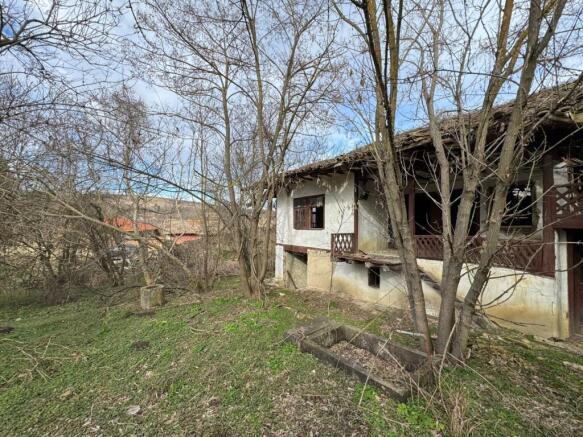 Side perspective of the old house showing white plaster walls, wooden balcony, and surrounding bare trees.