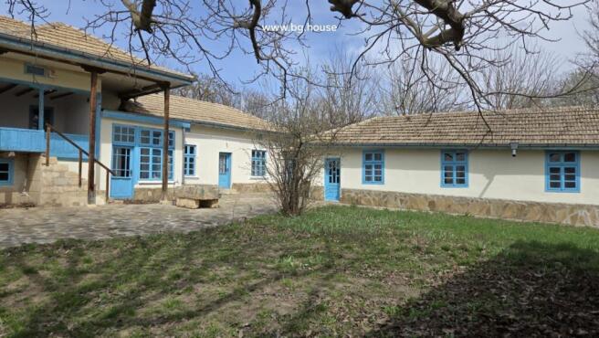 Stone paved courtyard with grass patches and traditional house walls featuring blue framed windows and doors.