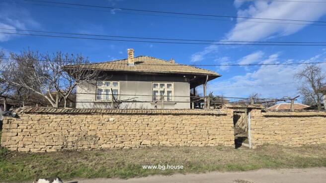 Front facade of Bulgarian house behind stone wall with leafless tree in yard