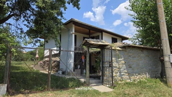 Front view of a traditional Bulgarian house with a gated entrance and stone wall under a blue sky