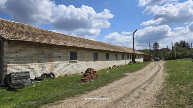 Exterior view of a long white brick farm building with a tiled roof along a dirt road in Osikovo village