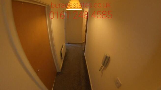 Narrow carpeted hallway with neutral walls, ove...