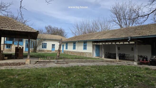 Exterior view of a traditional Bulgarian house with blue doors and windows and a tiled roof surrounded by leafless trees.