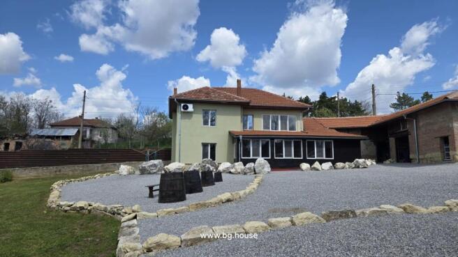 Two-storey house with green exterior walls and red tiled roof surrounded by gravel yard and stone borders