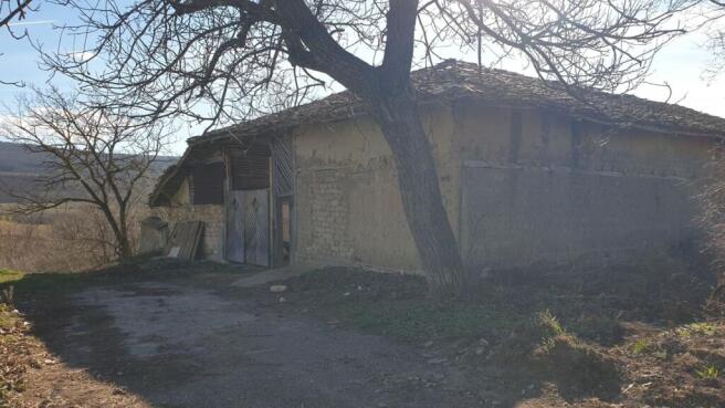 View of a large rustic outbuilding featuring wooden doors and mud brick walls, surrounded by bare trees