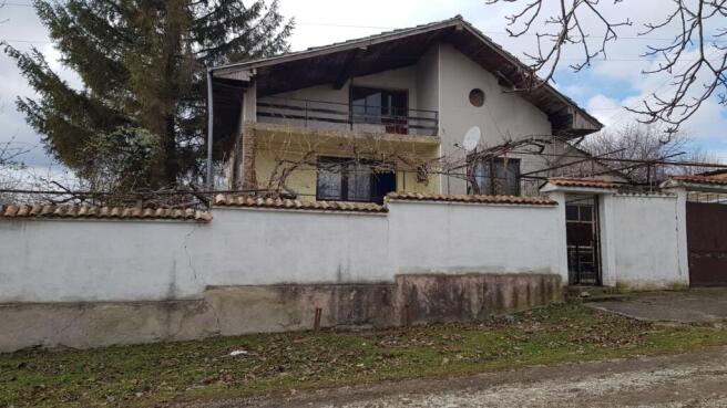 Front facade of a two-storey Bulgarian house with balcony and white garden wall