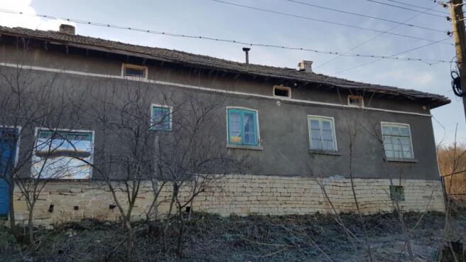 Front side of a Bulgarian village house showing stone foundation and plastered walls with multiple windows