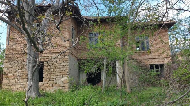 Two-storey rural house with brick upper floor and stone lower floor, surrounded by trees