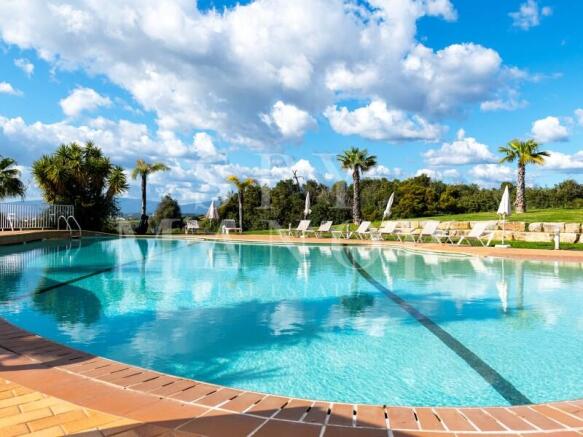Luxury resort swimming pool at Pestana Residences in Lagoa, Algarve. Surrounded by sun loungers, palm trees, and lush green golf resort landscaping.