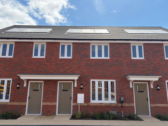 Two identical brick townhouses with gray doors and white-framed windows stand under a bright blue sk