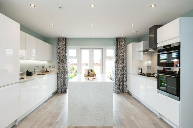 A modern white kitchen with a marble island in the foreground and large windows with patterned curta