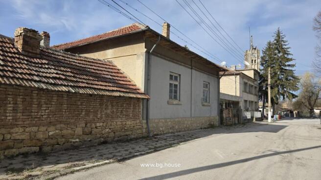 Side exterior view of a stone and brick house with a tiled roof and an adjacent brick wall along the street.