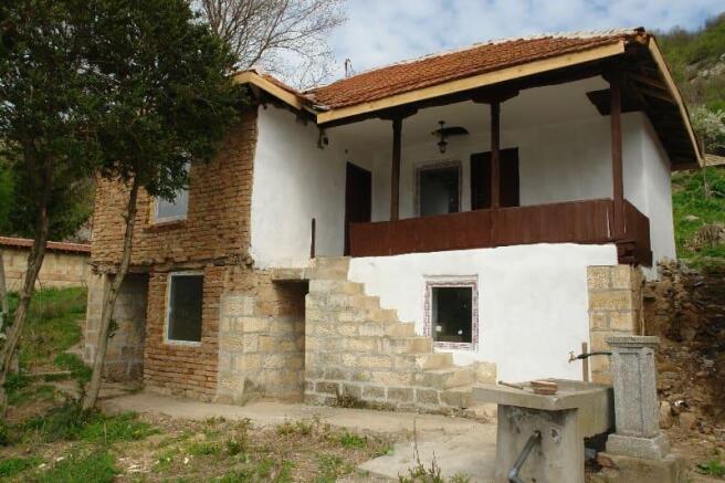 Rural Bulgarian house showing porch with wooden railing, stone stairs, and tiled roof