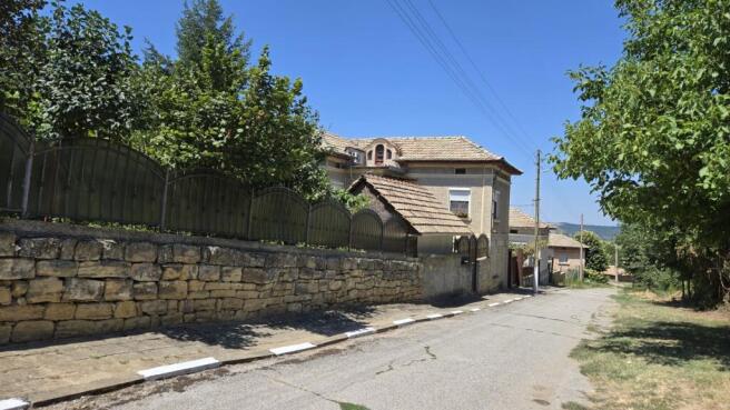 Stone wall topped with metal fencing enclosing the garden area beside the Bulgarian house.