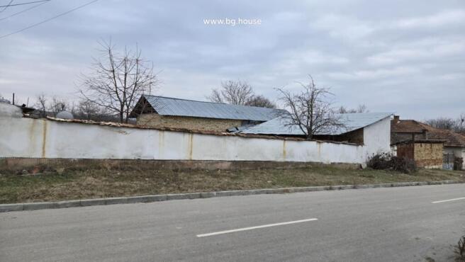 Metal roofed barn behind a white boundary wall in Katselovo village
