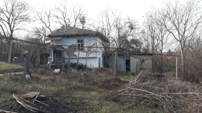 View of a small traditional Bulgarian house with peeling white walls and a tiled roof in a natural garden setting