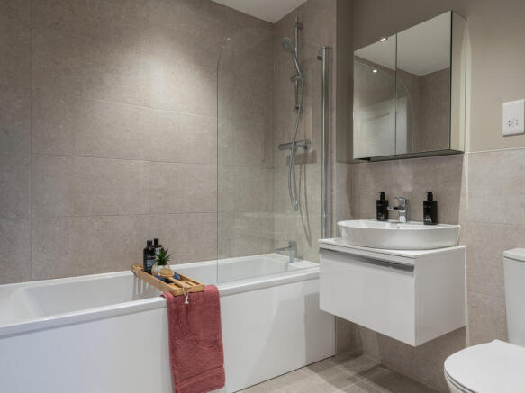 Family bathroom with a nice sized bath, sink, toilet and a mirror. White and grey tones