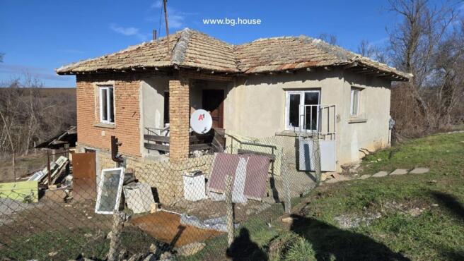 Side perspective of a Bulgarian rural house showing stone foundation and brick walls under clear blue sky