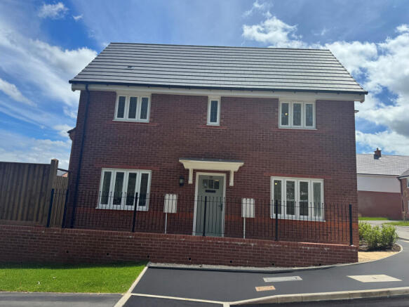 A modern red brick house with white-trimmed windows stands behind a low brick wall and black fence