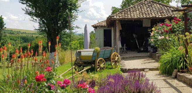 Rustic outbuilding with tiled roof next to vibrant garden flowers and green trees