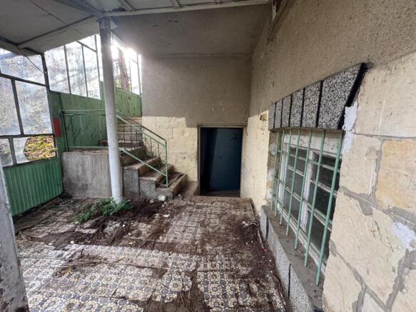 Covered entrance showing patterned tiled floor, stairs leading to upper and lower levels, and barred windows