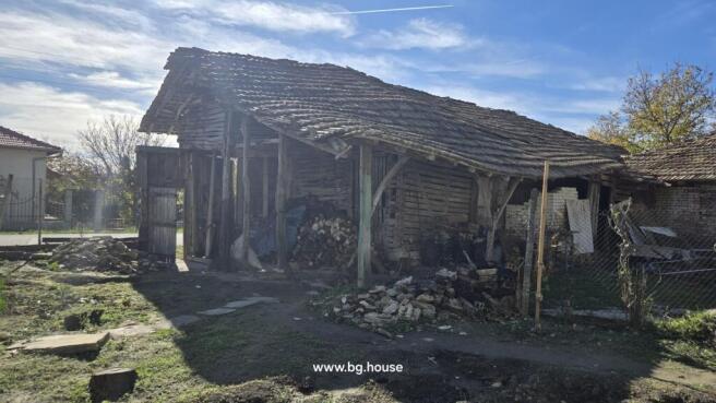 Rustic wooden barn with open sides and tiled roof, used for storage in the village property yard