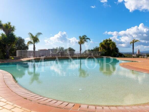 Large outdoor swimming pool at Pestana Residences golf resort in Lagoa, Algarve. Scenic sunny resort view with palm trees and blue sky.