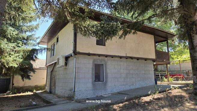 View of the rear corner of the house showing concrete block lower walls and plastered upper walls, partially shaded by tall trees.
