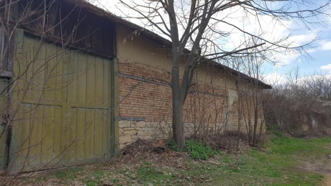 Side view of a brick building with a large green wooden door and leafless branches