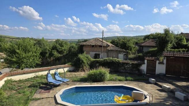 Outdoor swimming pool with clear blue water and two blue double sun loungers set on stone paving near garden greenery.