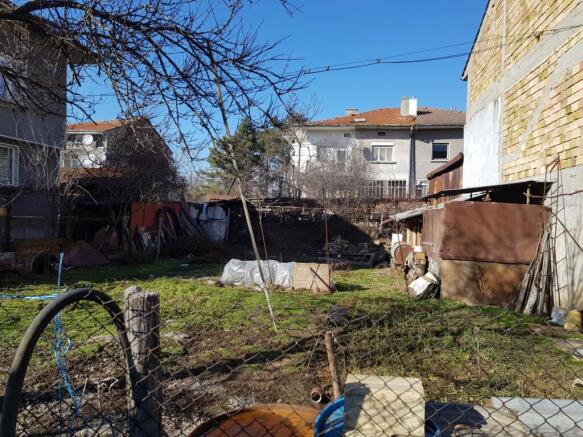View of fenced grassy building land with garden structures and bare trees in Popovo, Bulgaria