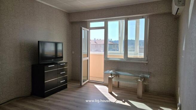 Spacious living room showing a TV on a black chest of drawers, a glass coffee table, and an open door to the balcony.